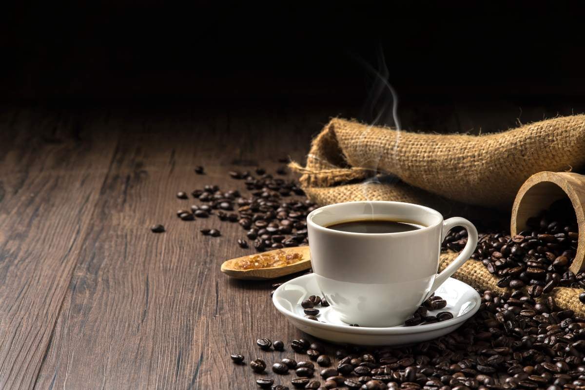 Poza de cover. Cum se face cafeaua la ibric - pasi_Ceasca alba cu cafea, boabe de cafea, sac, bol si lingura de lemn, masa, decor